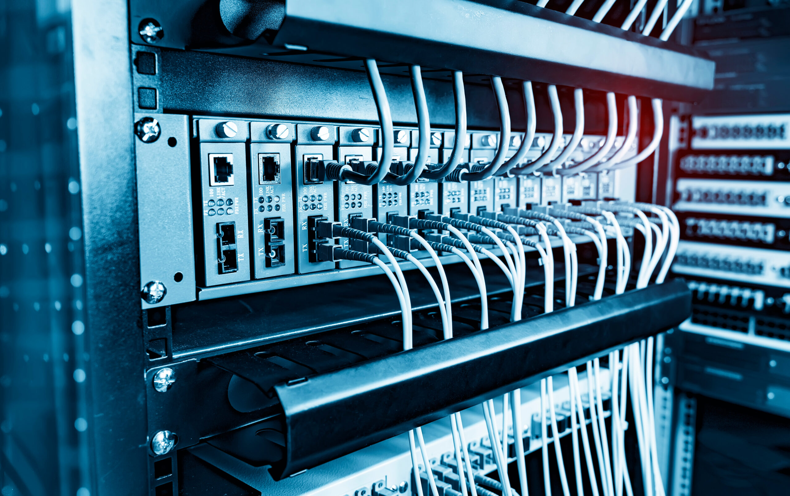 Data center server rack with fiber optic converters and organized network cabling in blue lighting.